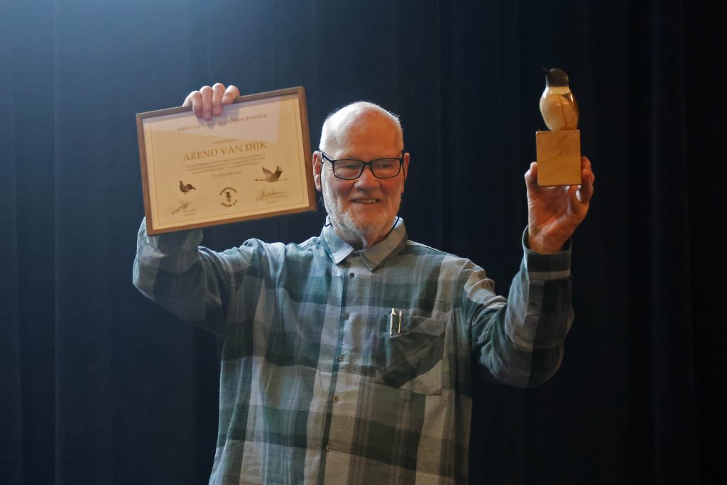 Trots toont Arend van Dijk zijn oorkonde met de FRED VAN VEMDEN ONDERSCHEIDING en het beeldje van de Roodborsttapuit